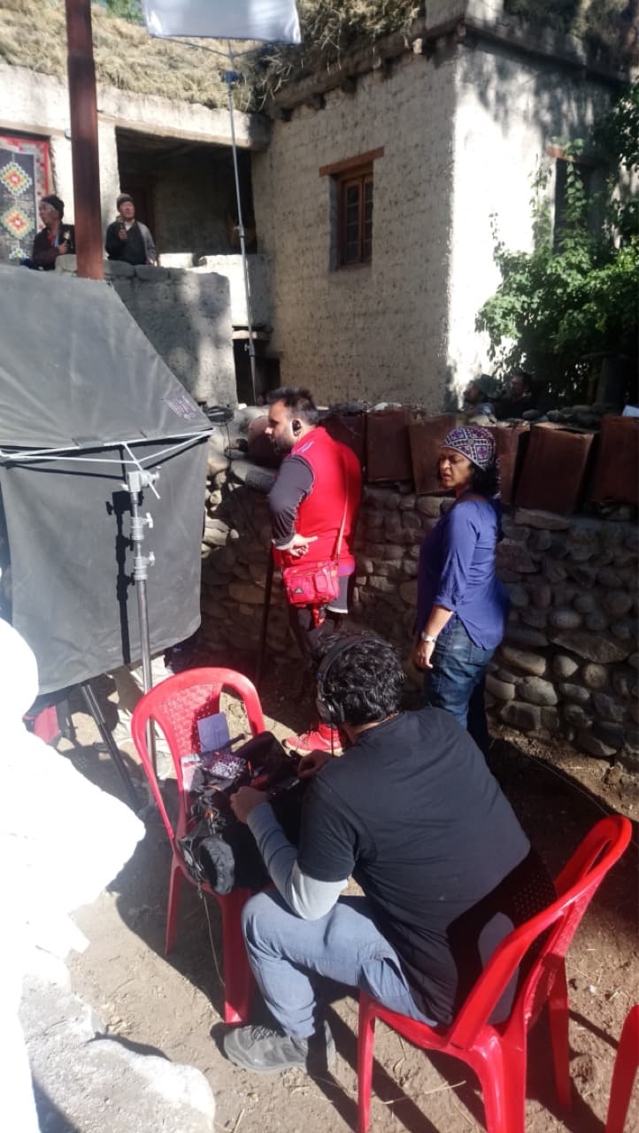 Film crew setting up reflectors, lighting flags, and sound recording gear in a traditional stone-walled courtyard