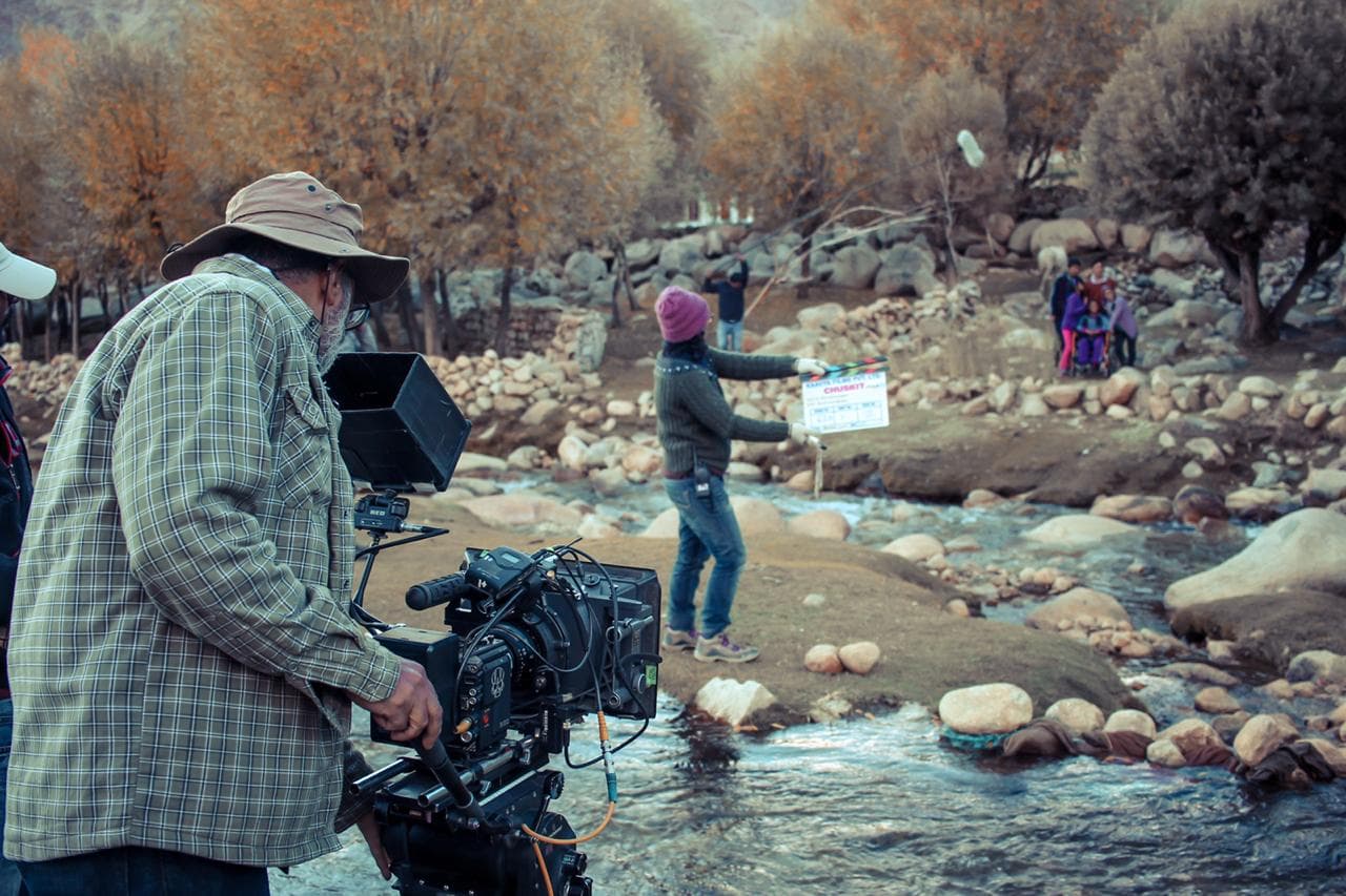 Cinematographer Arvind Kannabiran operating a RED camera on a tripod across a stream as a clapperboard marks the scene