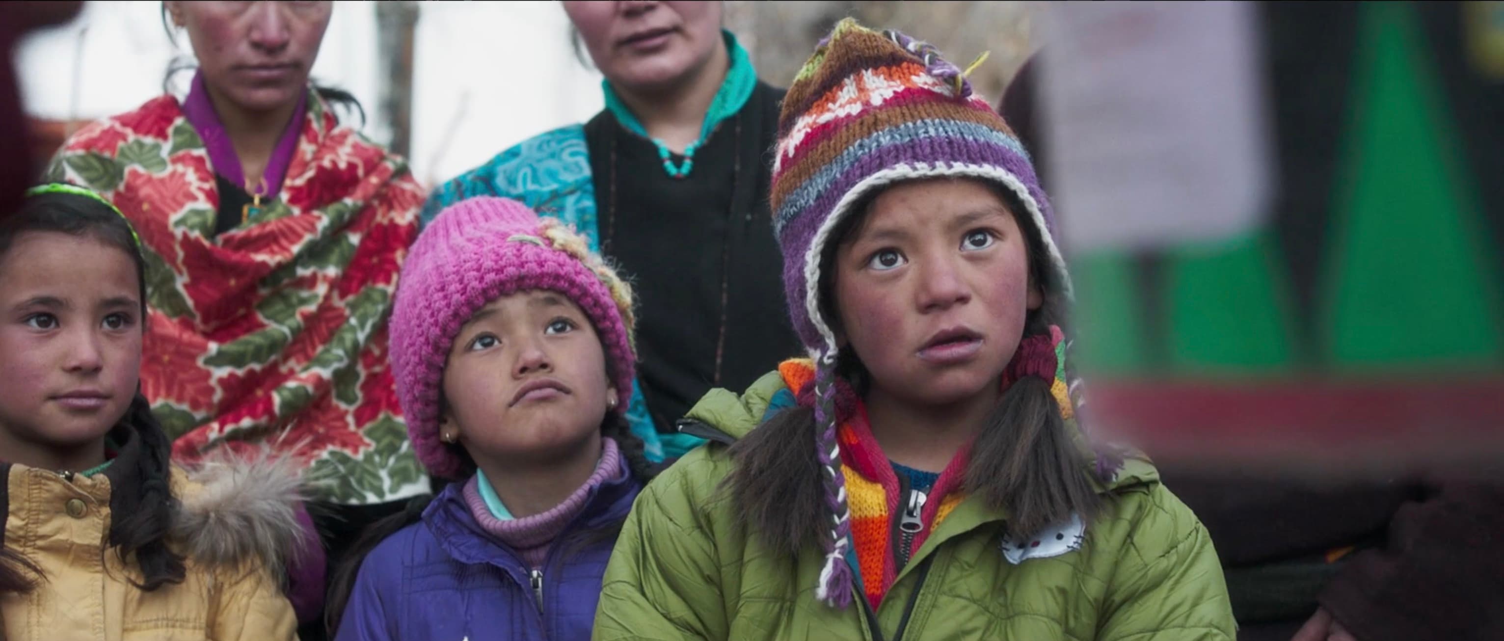 Close-up of Chuskit wearing a colorful knit beanie and green jacket, looking up with wonder and determination