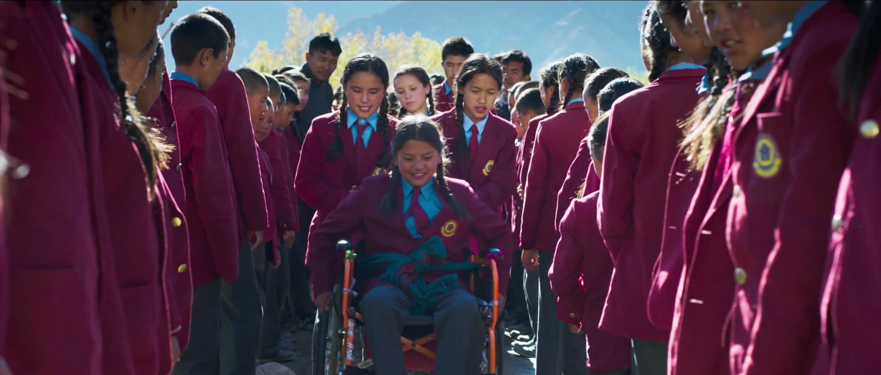 Chuskit rolling proudly in her wheelchair through a welcoming corridor of applauding schoolmates wearing maroon uniforms